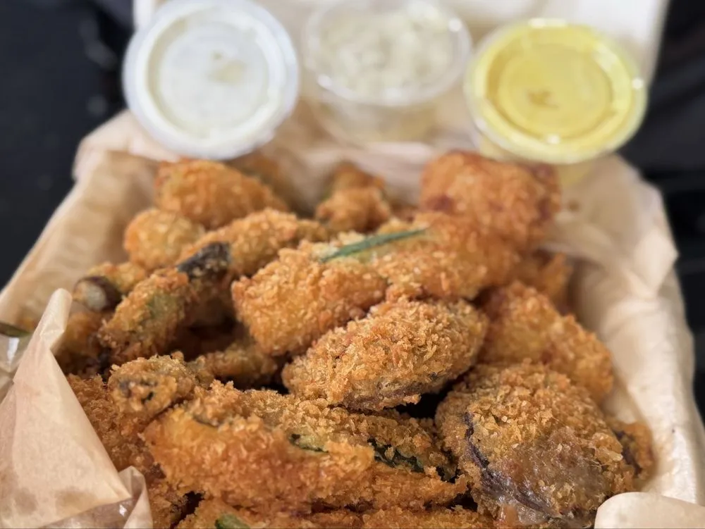 A basket of panko-fried vegetables (sweet potato, zucchini, asparagus and onion rings) beside dipping sauces.